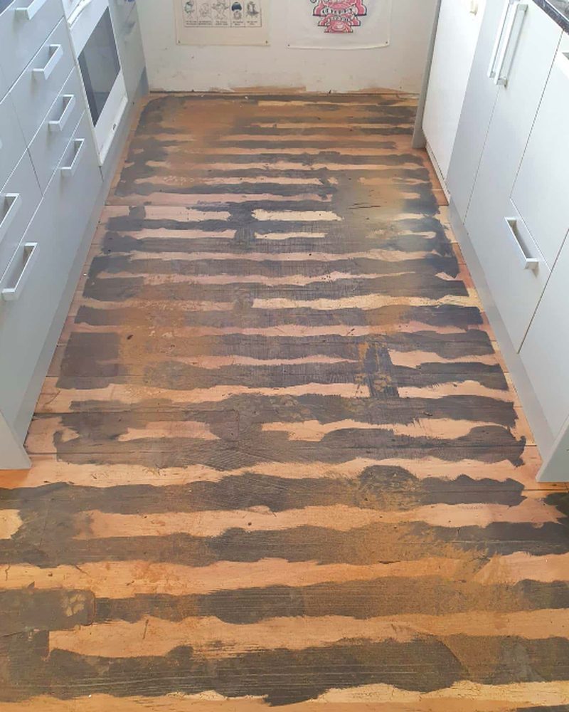 Kitchen floorboards stripped back with old dark coating still patched across the timber before sanding